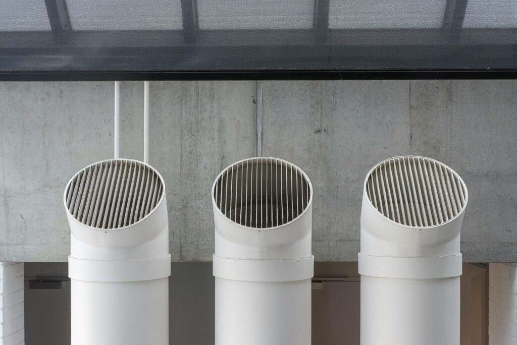 commercial-plumbing Three white industrial ventilation pipes aligned on concrete wall.